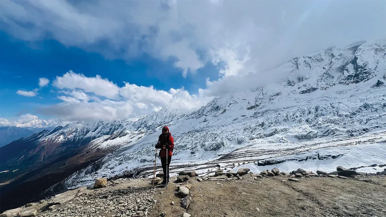 A trekker in a red jacket on a ridge above the glaciers of the Manaslu region